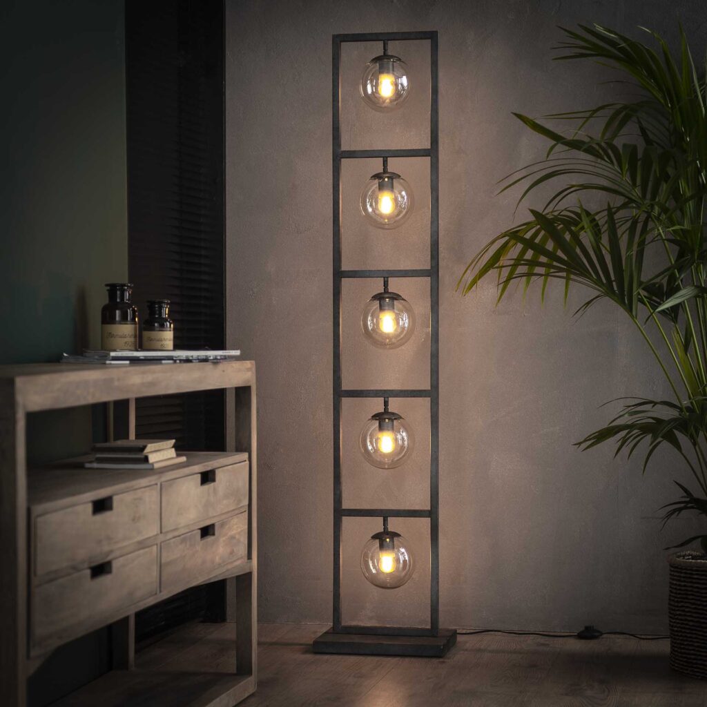 Industriele staande lamp met ronde glazen bollen naast houten meubel en groene plant in interieur Belga Meubel Brugge