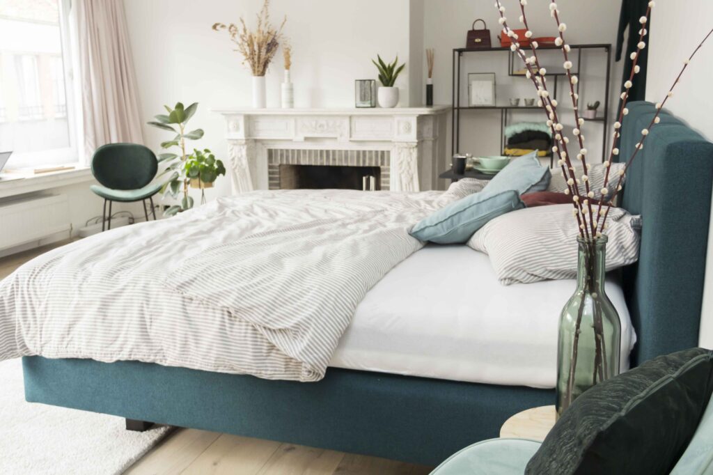 Moderne slaapkamer met blauw bedframe, gestreept beddengoed en decoratieve elementen bij Belga Meubel Brugge