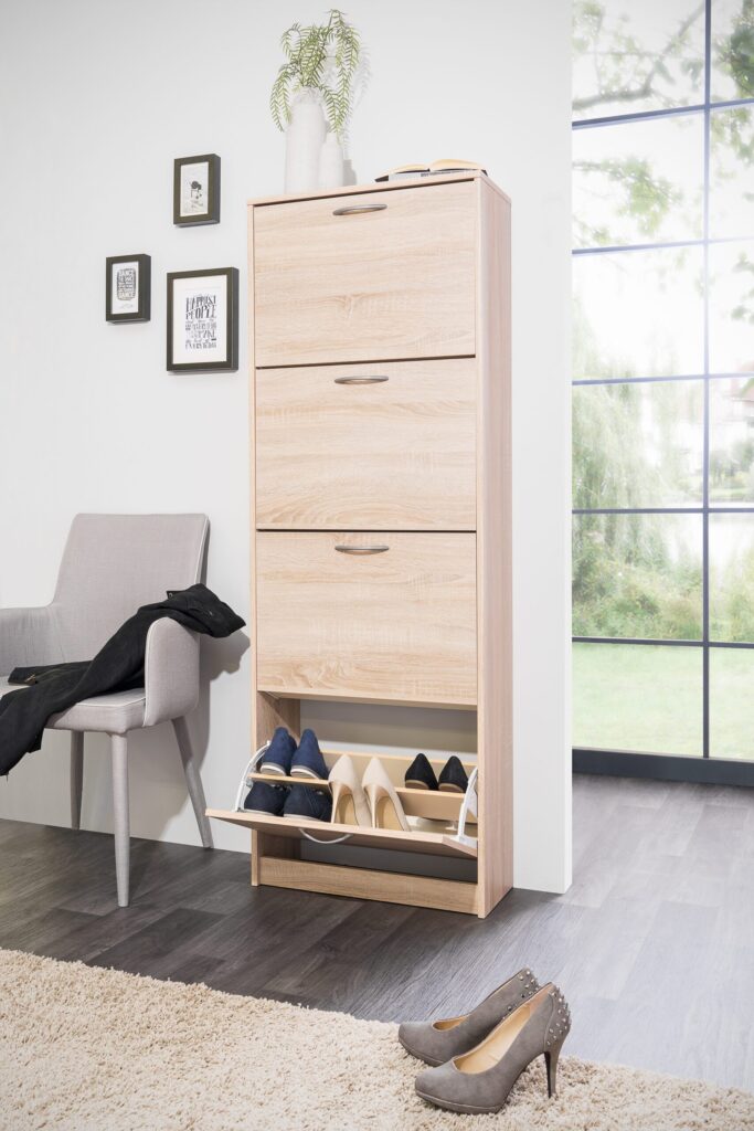 Schoenenkast van licht hout met open vak en verschillende schoenen, naast een grijze stoel met jas, Belga Meubel Brugge