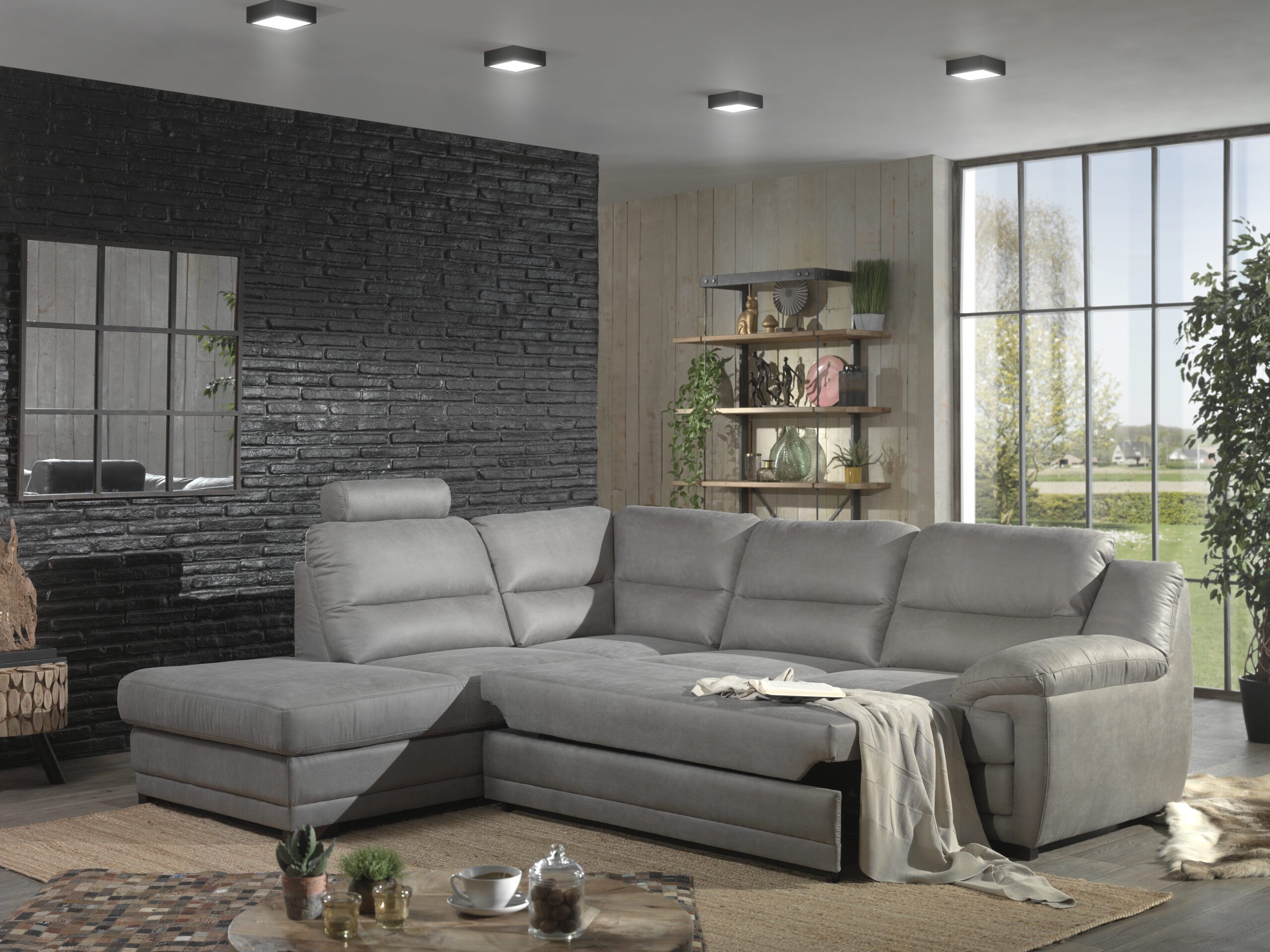 grijze hoekzetel met relaxfunctie in moderne woonkamer met zwarte stenen muur en grote raam bij Belga Meubel Brugge