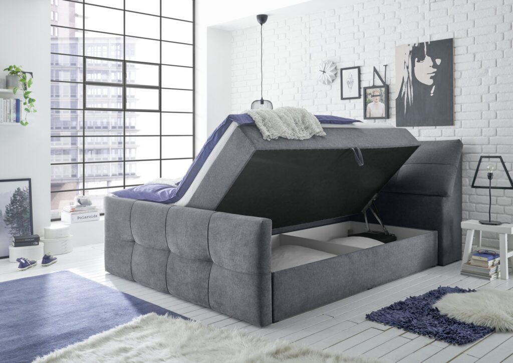 Moderne grijze boxspring bed met opbergruimte in lichte slaapkamer met witte bakstenen muur bij Belga Meubel Brugge