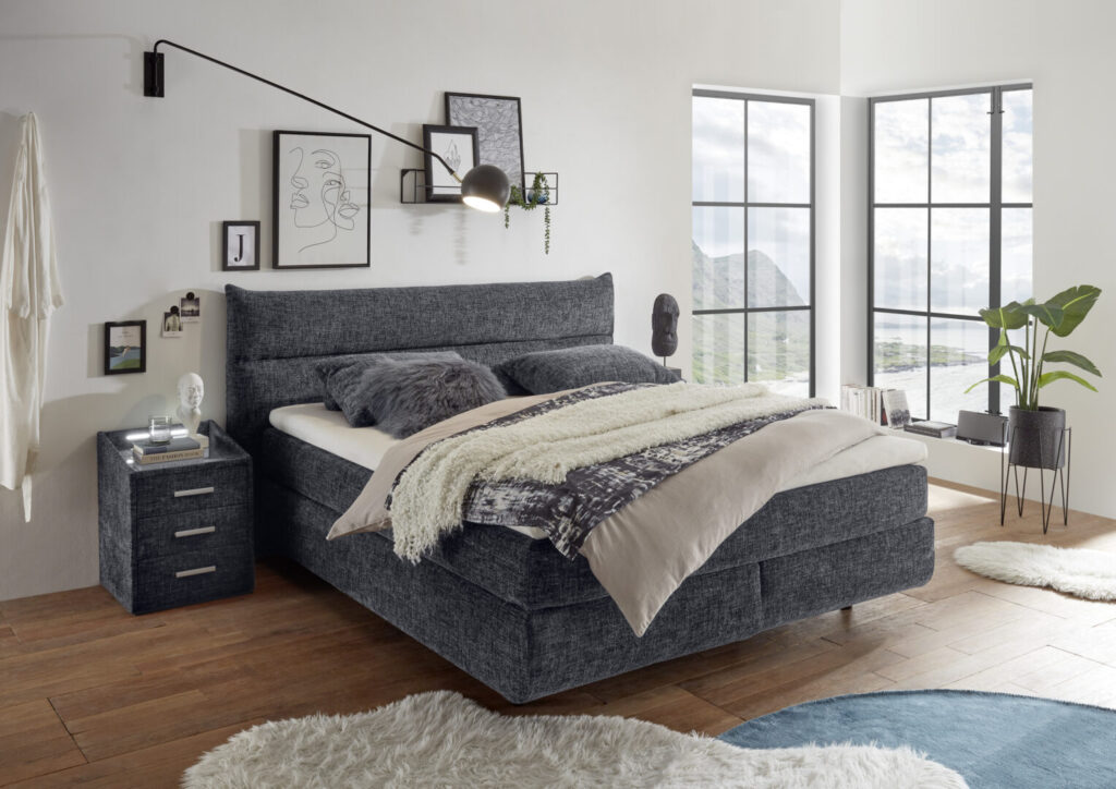 Slaapkamerinrichting met grijs boxspringbed en nachtkastje van Belga Meubel Brugge in moderne woonkamer met grote ramen
