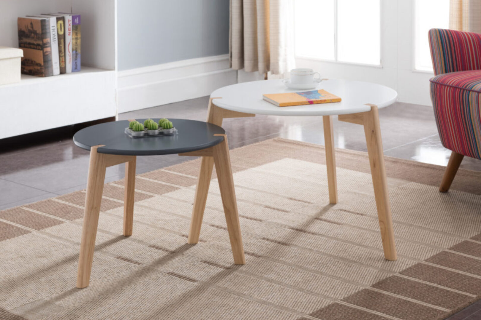 Set van twee ronde salontafels met houten poten, een zwarte en een witte, in een woonkamer met tapijt en gestreepte fauteuil, verkrijgbaar bij Belga Meubel Brugge
