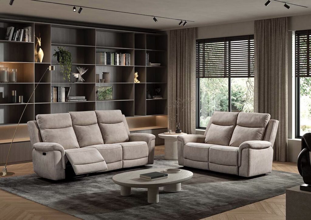Twee beige relaxzetels en bank in moderne woonkamer met grote boekenkast en raam, meubels van Belga Meubel Brugge