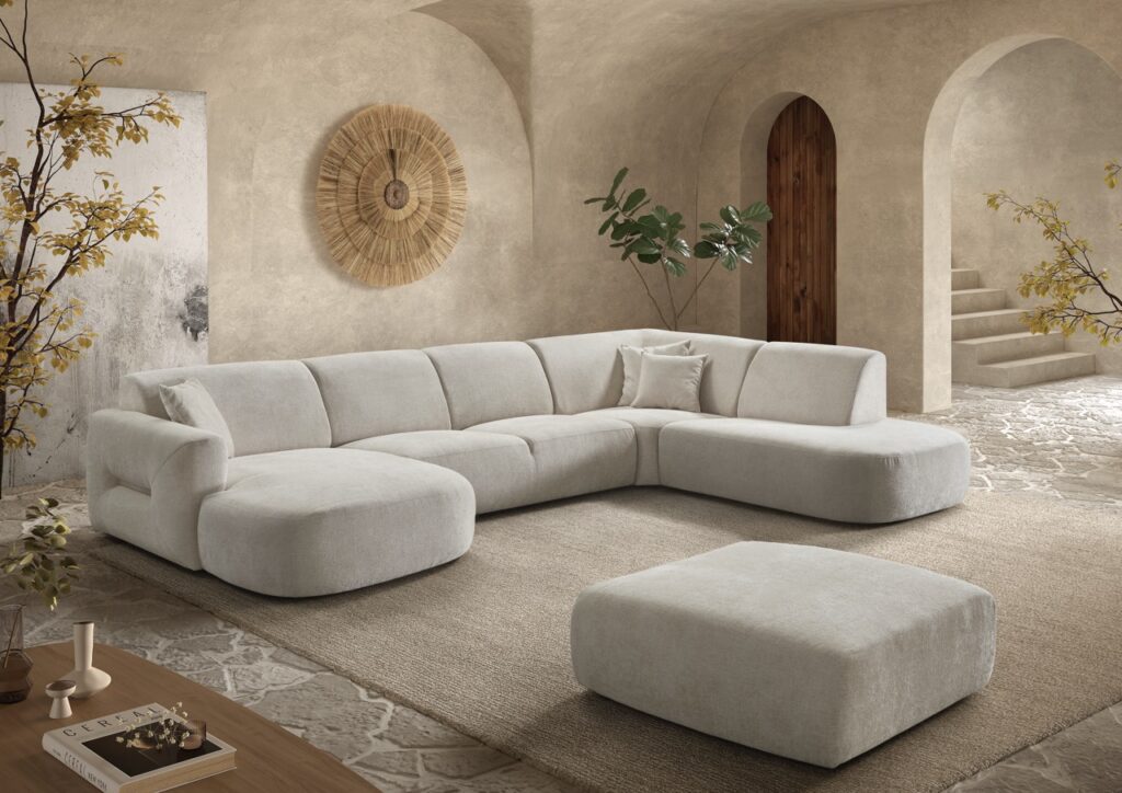Luxe beige hoekbank en poef in een natuurlijke woonkamer met planten en zachte tinten, verkrijgbaar bij Belga Meubel Brugge