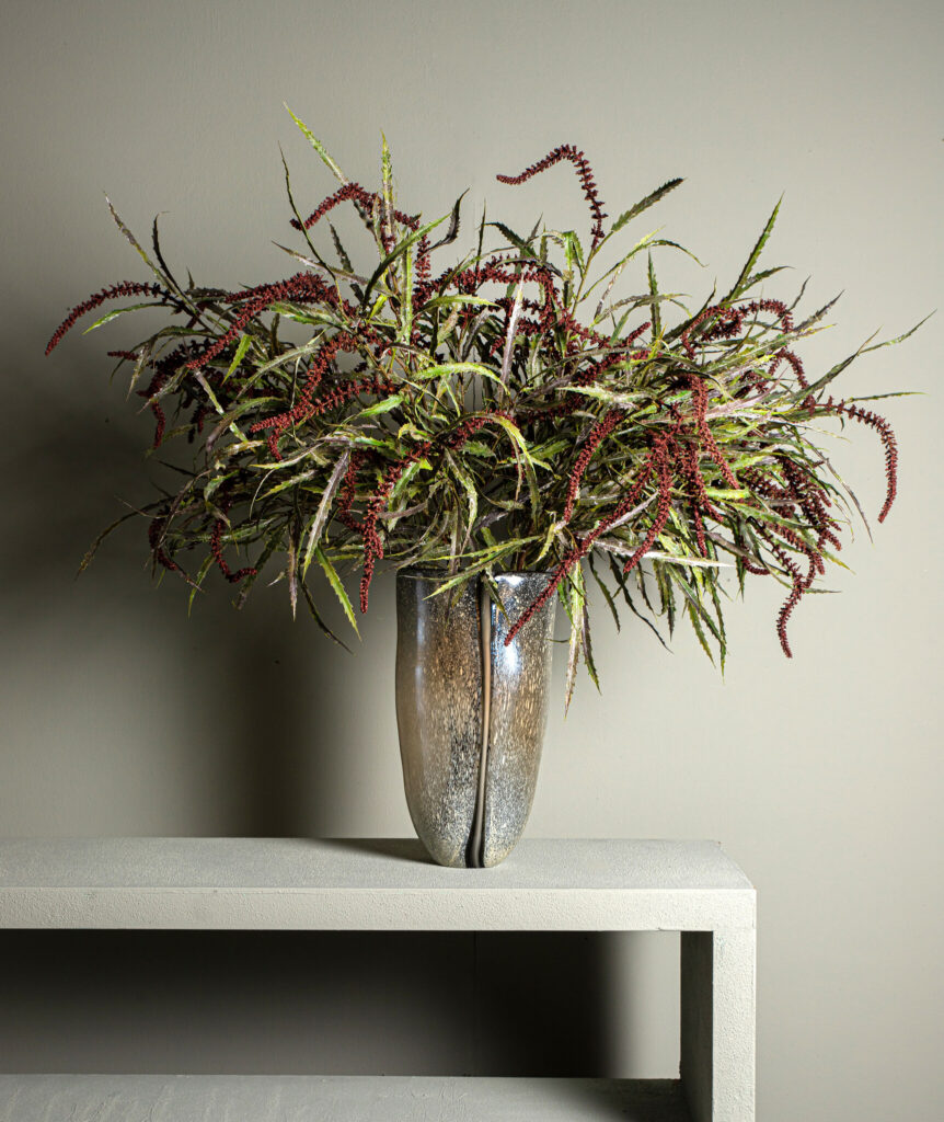 Moderne glazen vaas met decoratieve rode en groene takken op wit blad bij Belga Meubel Brugge