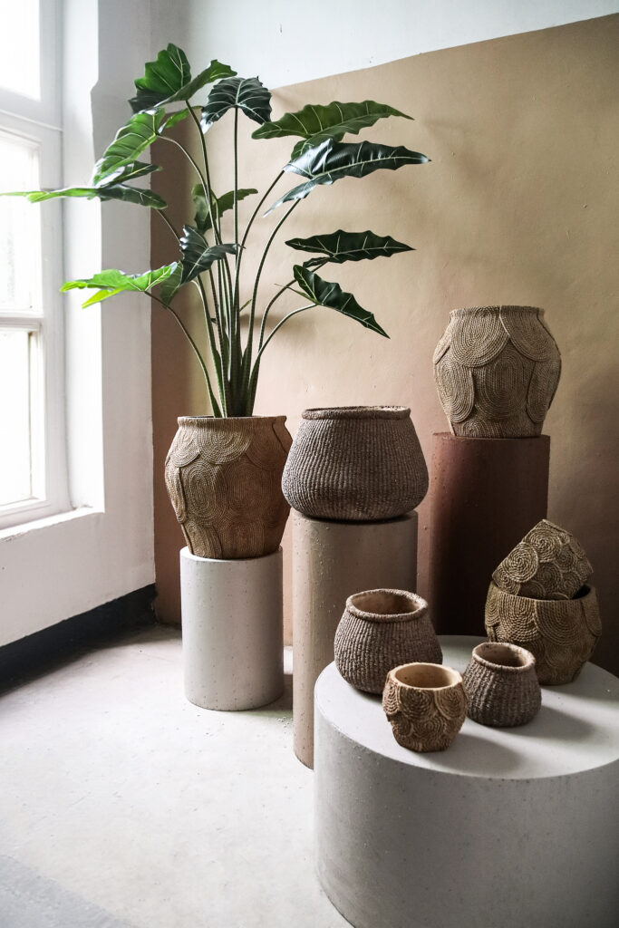 Grote groene kamerplant in rieten pot met diverse natuurlijke rieten manden in lichte kamer bij Belga Meubel Brugge