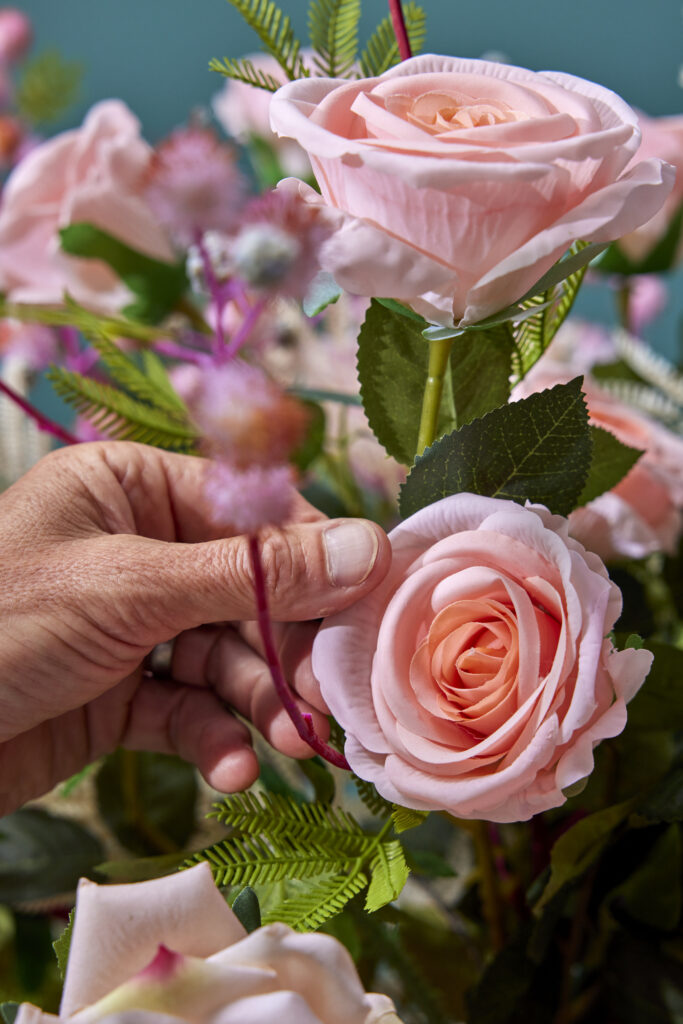 Hand die een boeket met roze kunstrozen en groen blad vastneemt, verkrijgbaar bij Belga Meubel Brugge