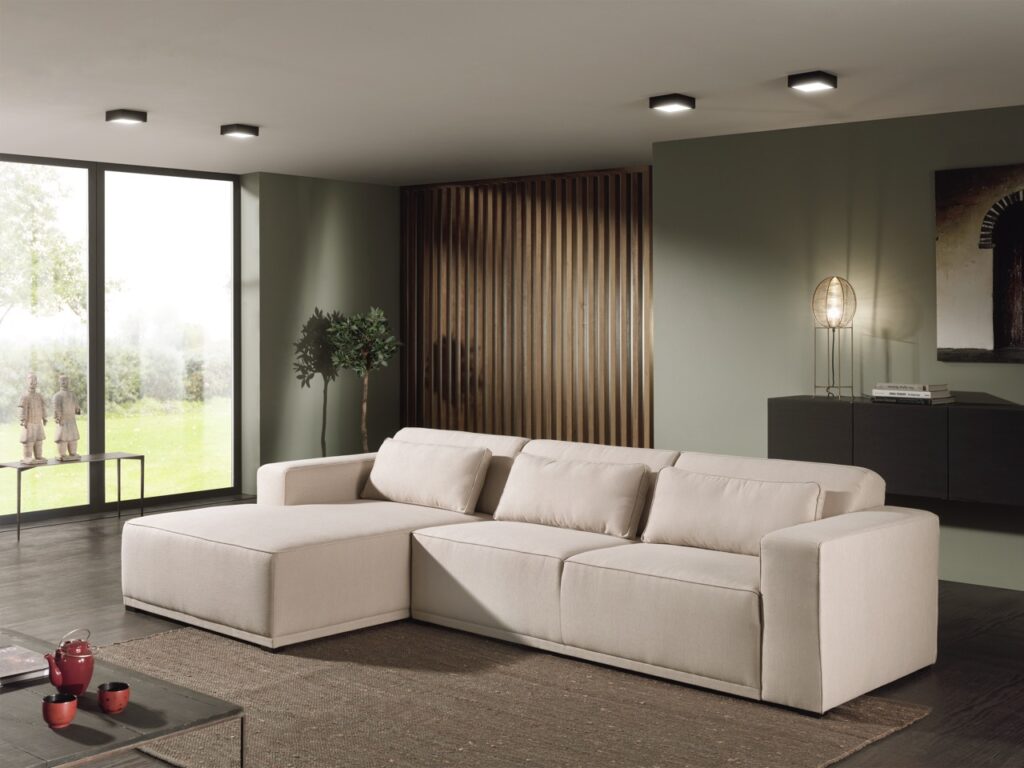 Lichtbeige hoekbank in moderne woonkamer met groene muur en houten decoratie bij Belga Meubel Brugge