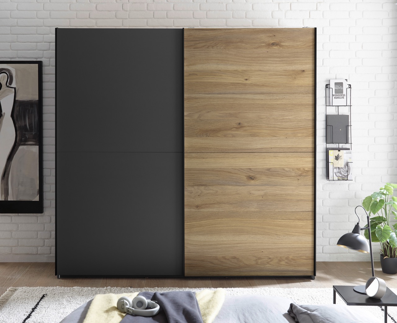 Moderne kast met twee schuifdeuren, één antraciet grijs en één in houtlook, in een slaapkamer met witte bakstenen muur