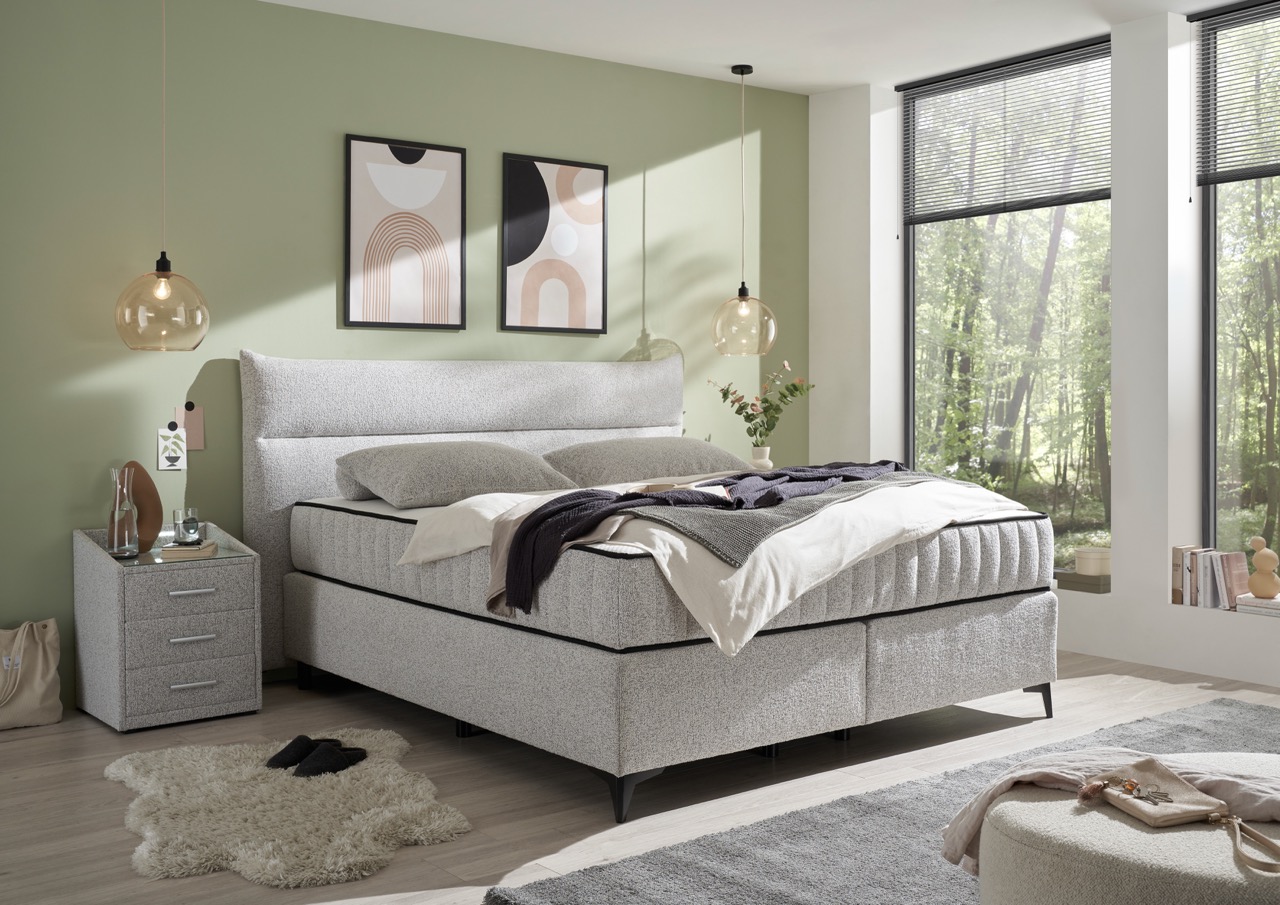 Modern boxspringbed met grijze stof bekleding in lichte slaapkamer met groene muur en grote ramen