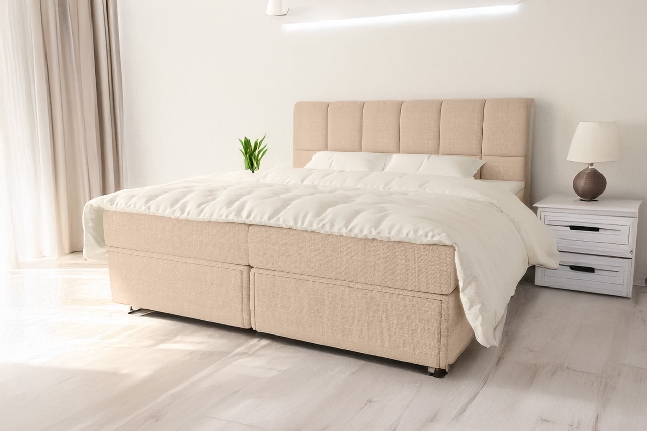 Beige gestoffeerd boxspringbed met wit beddengoed in lichte slaapkamer met wit nachtkastje en lamp