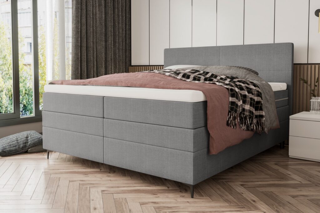 Modern grijs gestoffeerd boxspringbed met roze dekbed en geruite deken in stijlvolle slaapkamer bij Belga Meubel Brugge